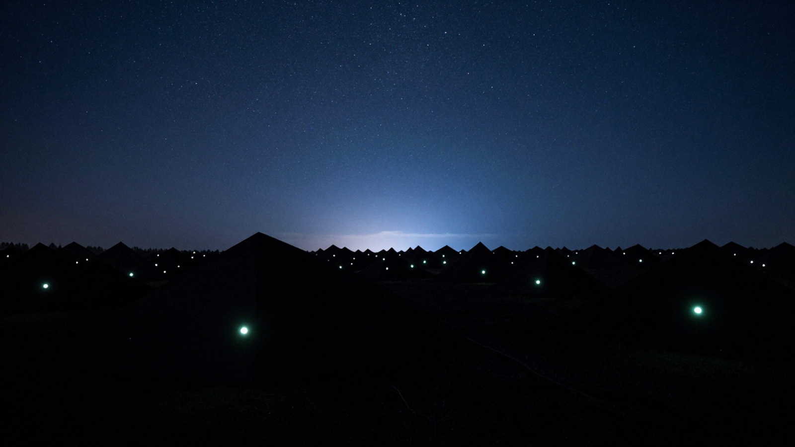 Stylized illustration: abstract dark volumes speckled with small lights under a dense star field and a band of blue twilight.